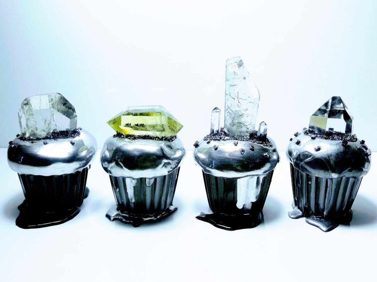 Four GemCake sculptures in a row, black cake forms topped with clear and green cut quartz