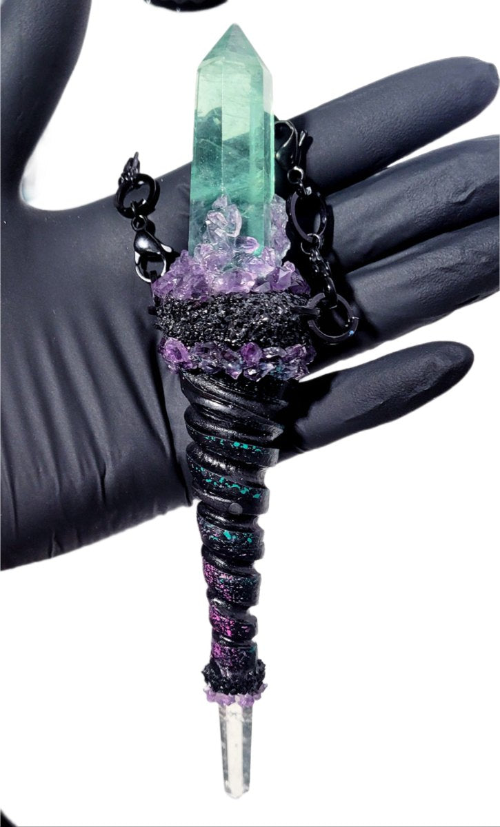 Gloved hand holding a green aura quartz point set in blackened silver