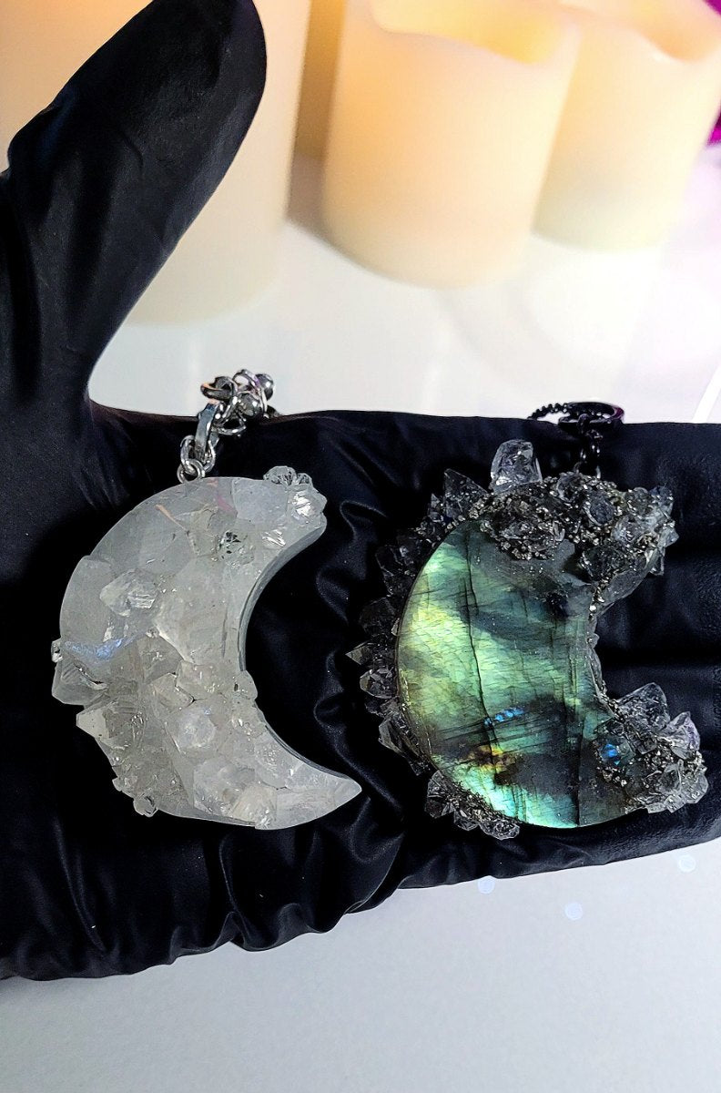 Gloved hand holding two cut crescent moons in druzy quartz and labradorite