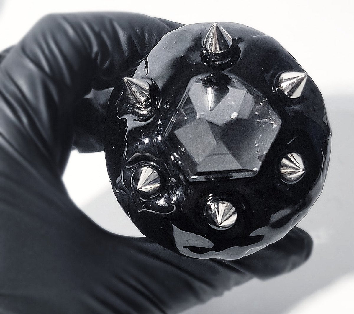 Gloved hand holding a spiked black sphere set with a faceted stone