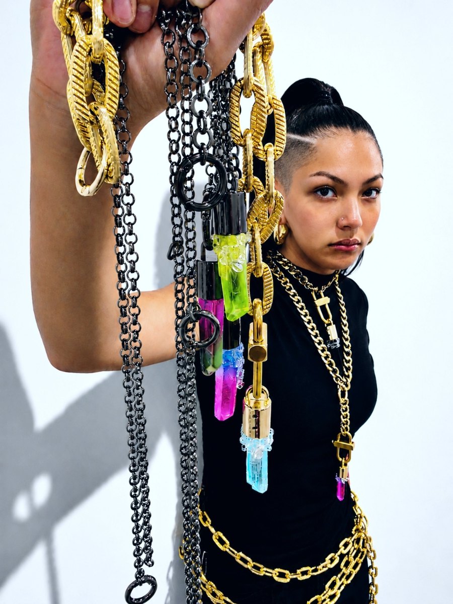Gold and gunmetal chains with aura quartz pendants held up against a white studio wall